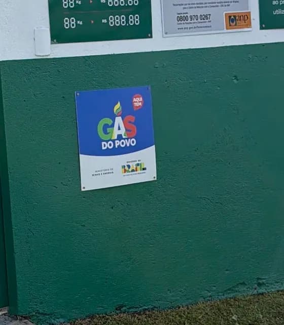 Placa do Gás do Povo com a frase Aqui tem, presa no muro verde da Lino Gás, ao lado do portão